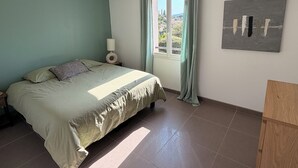 Une chambre à coucher avec un lit, une table de chevet, une lampe, une fenêtre avec des rideaux et un tableau au mur.
