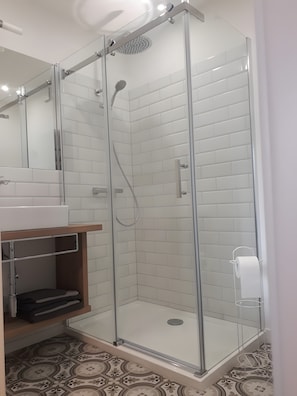 Ein modernes Badezimmer mit einer gläsernen Dusche, weißen Fliesenwänden, einem Waschbecken mit Spiegel und gestreiften Bodenfliesen.