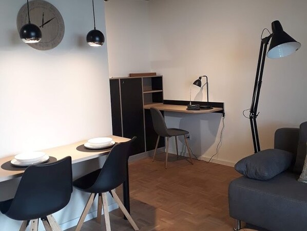A compact living space with a dining table, two chairs, a desk with a chair, a sofa, and a floor lamp.