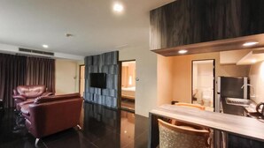 A modern hotel room with a leather sofa, a flat-screen TV, a wooden dining table, and a mirror. - Avana Bangkok Hotel & Convention Centre (Bangkok)