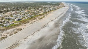 An aerial view of a coastal town with a long beachfront, residential buildings, and a clear sky. - Just Beachy l Steps to Beach l Walk to Restaurants (St. Augustine)