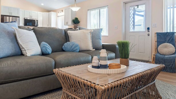 A living room with a grey sofa, a wooden coffee table, and a wicker chair. - Just Beachy l Steps to Beach l Walk to Restaurants (St. Augustine)