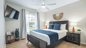 A modern bedroom with a bed, bedside tables, a ceiling fan, a TV, and a window with curtains. - Just Beachy l Steps to Beach l Walk to Restaurants (St. Augustine)