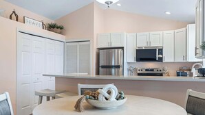 A modern kitchen with white cabinets, stainless steel appliances, and a central island with a bowl of decorative items. - Just Beachy l Steps to Beach l Walk to Restaurants (St. Augustine)