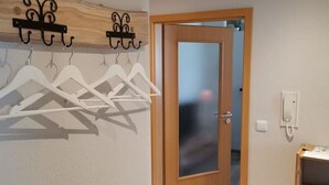 Un couloir avec une porte en bois, un porte-manteau avec des cintres blancs et un téléphone fixé au mur.