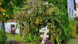 Un jardin avec une croix en bois, entouré de verdure et de fleurs.