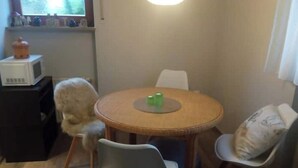 Un petit coin repas avec une table ronde, deux chaises, un four à micro-ondes posé sur une étagère et une fenêtre donnant sur un paysage agréable.