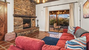 Una sala de estar acogedora con chimenea de piedra, sofás rojos y vistas al exterior a través de amplios ventanales correderas.