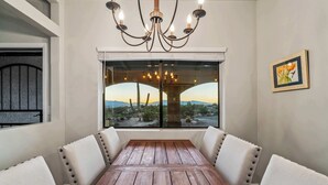 Comedor con mesa de madera y sillas tapizadas, una araña y vistas de un puente y paisaje a través de amplios ventanales.
