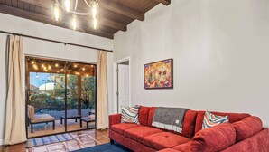 Una sala de estar con un sofá rojo, un tapete azul y un ventanal con cortinas.