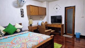 Une chambre à coucher comprenant un lit, un bureau, une chaise, un téléviseur, un ventilateur et une porte.