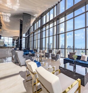 Un vaste espace salon doté de mobilier contemporain, de grandes fenêtres offrant une vue sur la ville et d’un design de plafond élégant.