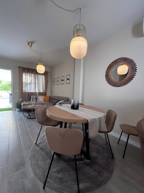 Uma área de refeições moderna com uma mesa redonda, cadeiras, luminárias pendentes e um espelho decorativo na parede.