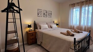 A bedroom with a bed, a nightstand, a lamp, a ladder, a chair, and a window with curtains.