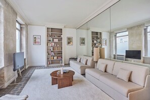 Ett vardagsrum med en beige soffa, ett soffbord, en bokhylla och en tv.