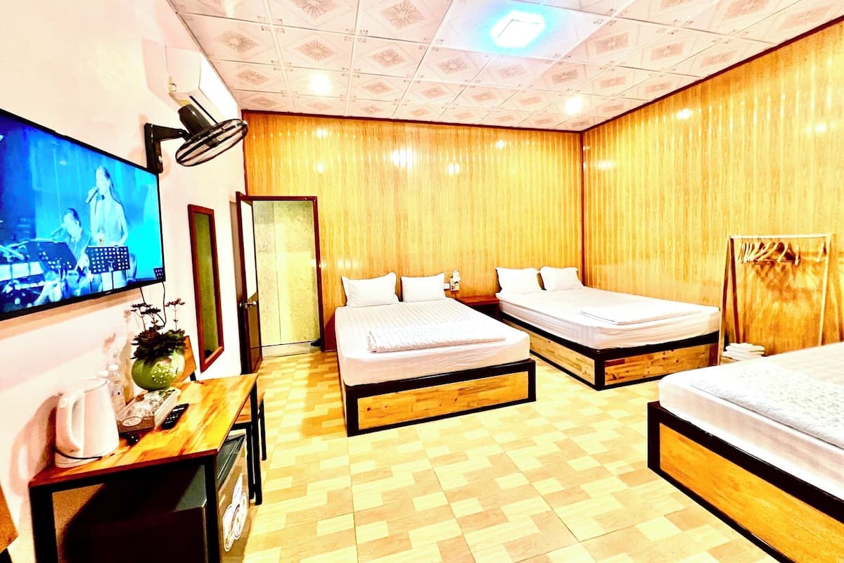 Une chambre d’hôtel avec deux lits, un téléviseur fixé au mur, un plancher en bois et une porte donnant sur une autre pièce.
