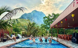 A swimming pool with people enjoying the water, surrounded by lush greenery and a mountainous backdrop. - Tràng An Dragon Homestay (Ninh Binh)