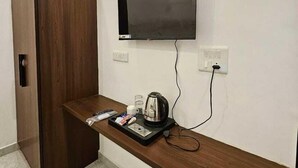 Une chambre d’hôtel avec une armoire en bois, un téléviseur à écran plat fixé au mur, une petite table avec une bouilloire, des verres et un plateau contenant divers articles.