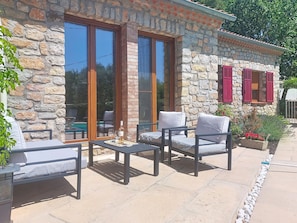 A stone building with large windows, outdoor seating, and a pool.