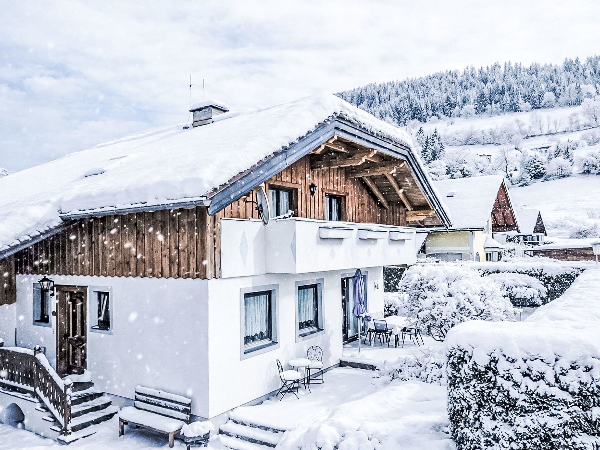 A wooden chalet with a balcony, a covered porch, and a view of snow-covered trees.