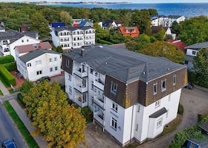 Un immeuble résidentiel à plusieurs étages, doté de balcons, d’une allée pavée et offrant une vue sur la mer.