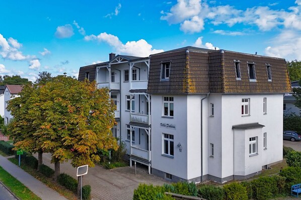 Ein mehrstöckiges Gebäude mit Balkonen, einem Schild mit der Aufschrift 'Villa Dakeim' und einem Baum im Vordergrund.