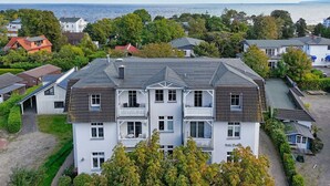 A multi-story building with a balcony, surrounded by trees and a view of the sea.