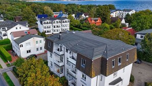 A multi-story residential building with balconies, a paved driveway, and a view of the sea.