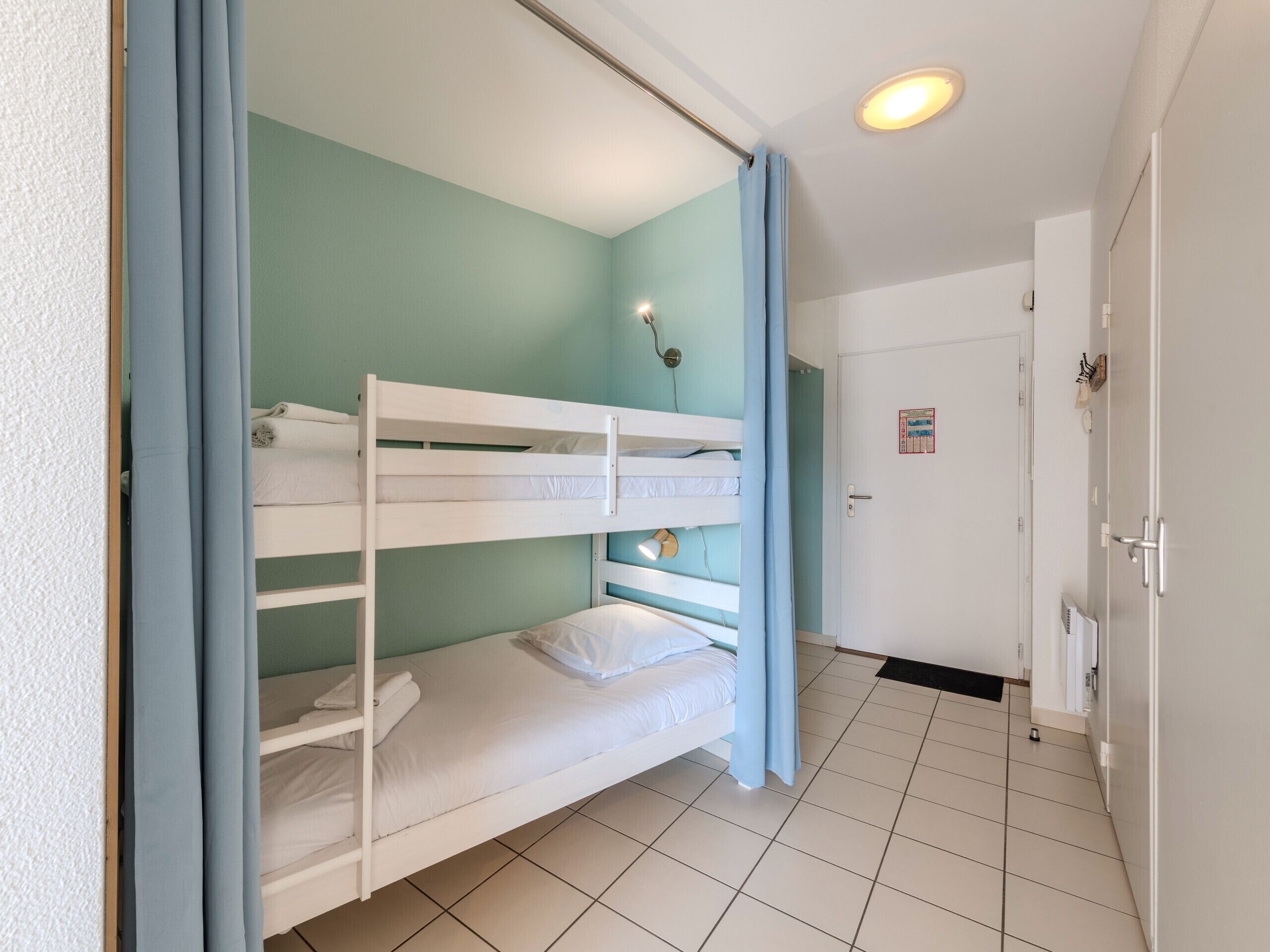 Dormitorio con literas, una puerta, un accesorio de iluminación y suelo de baldosas.