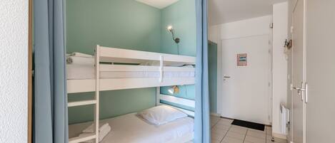 Dormitorio con literas, una puerta, un accesorio de iluminación y suelo de baldosas.