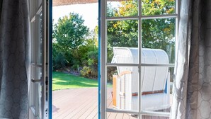 Un dormitorio con un ventanal grande, una silla de mimbre y vista a un jardín.