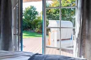 Ein Schlafzimmer mit einem großen Fenster, einem Korbstuhl und Blick auf einen Garten.