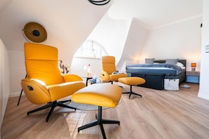 Ein modernes Schlafzimmer im Loft-Stil mit hohen Decken, einem großen Fenster, einem Bett, einem Schreibtisch und einem gelben Sessel.