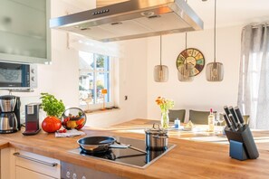 A modern kitchen with a stove, a coffee maker, a fruit bowl, and a vase with flowers.