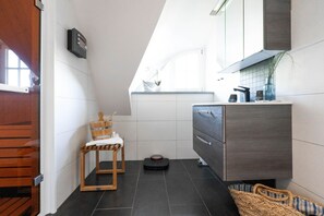 Ein modernes Badezimmer mit einem Holzstuhl, einem kleinen Waschbecken und einem dunklen Fliesenboden.