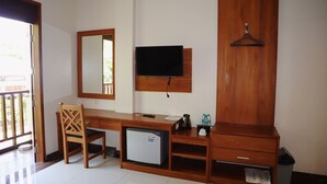 A hotel room with a wooden desk, a small refrigerator, a TV mounted on the wall, a wooden wardrobe, and a hanging coat rack. - Hotel Grand Papua Kaimana  (Krooy)
