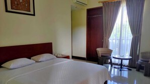 A hotel room with a large bed, a small table, wicker chairs, and a door leading to another room. - Hotel Grand Papua Kaimana  (Krooy)