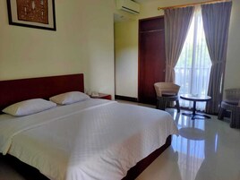 Habitación de hotel con una cama grande, una mesita pequeña, sillas de mimbre y una puerta que da a otra habitación.
