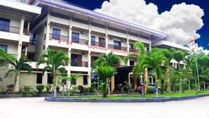 A multi-story hotel with balconies, a covered entrance, and a flag. - Hotel Grand Papua Kaimana  (Krooy)
