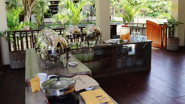 A buffet setup with multiple serving stations, a wooden table, and a view of lush greenery outside. - Hotel Grand Papua Kaimana  (Krooy)
