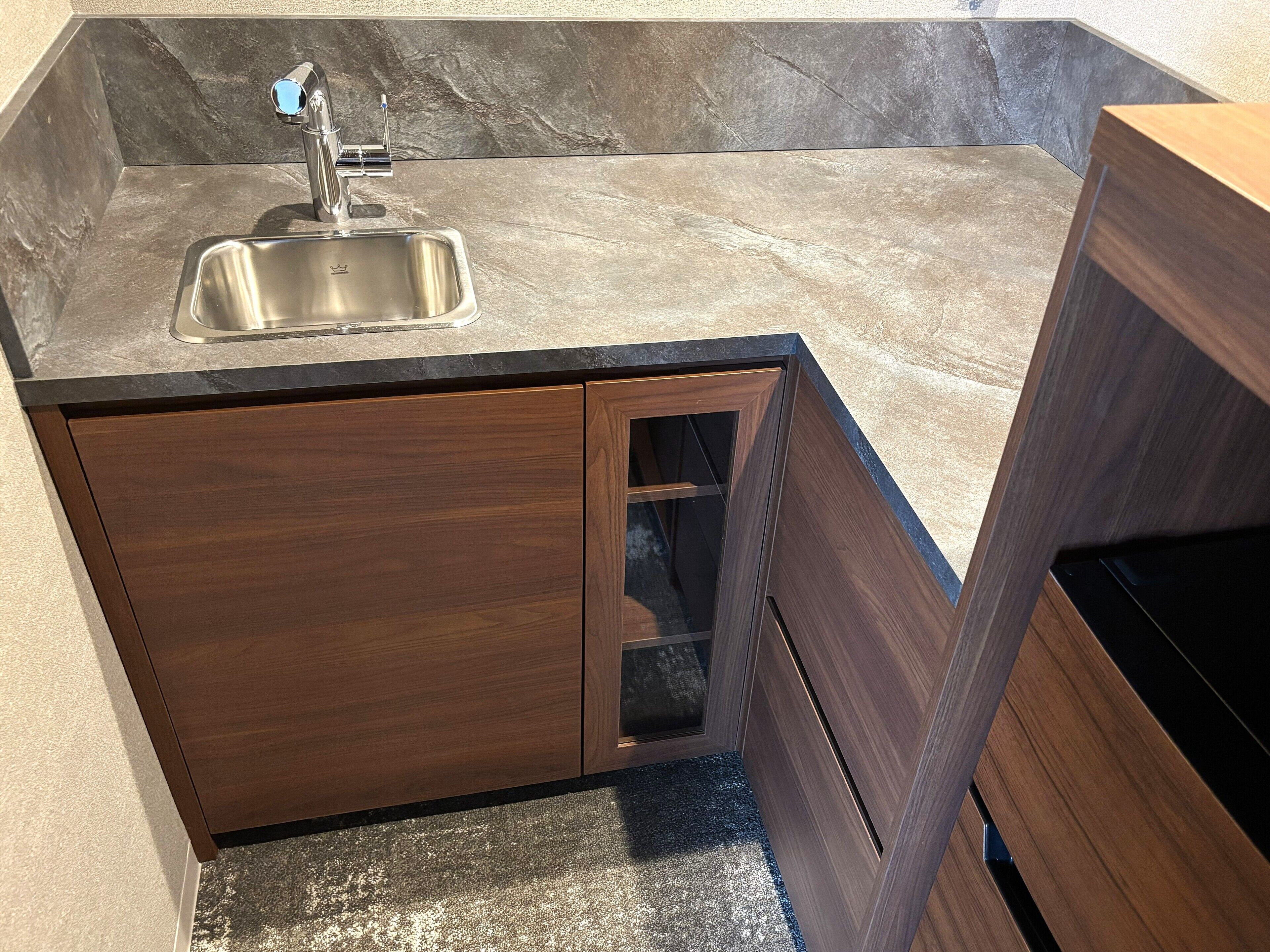 A modern kitchen with a stainless steel sink, dark wooden cabinets, and a marble countertop.
