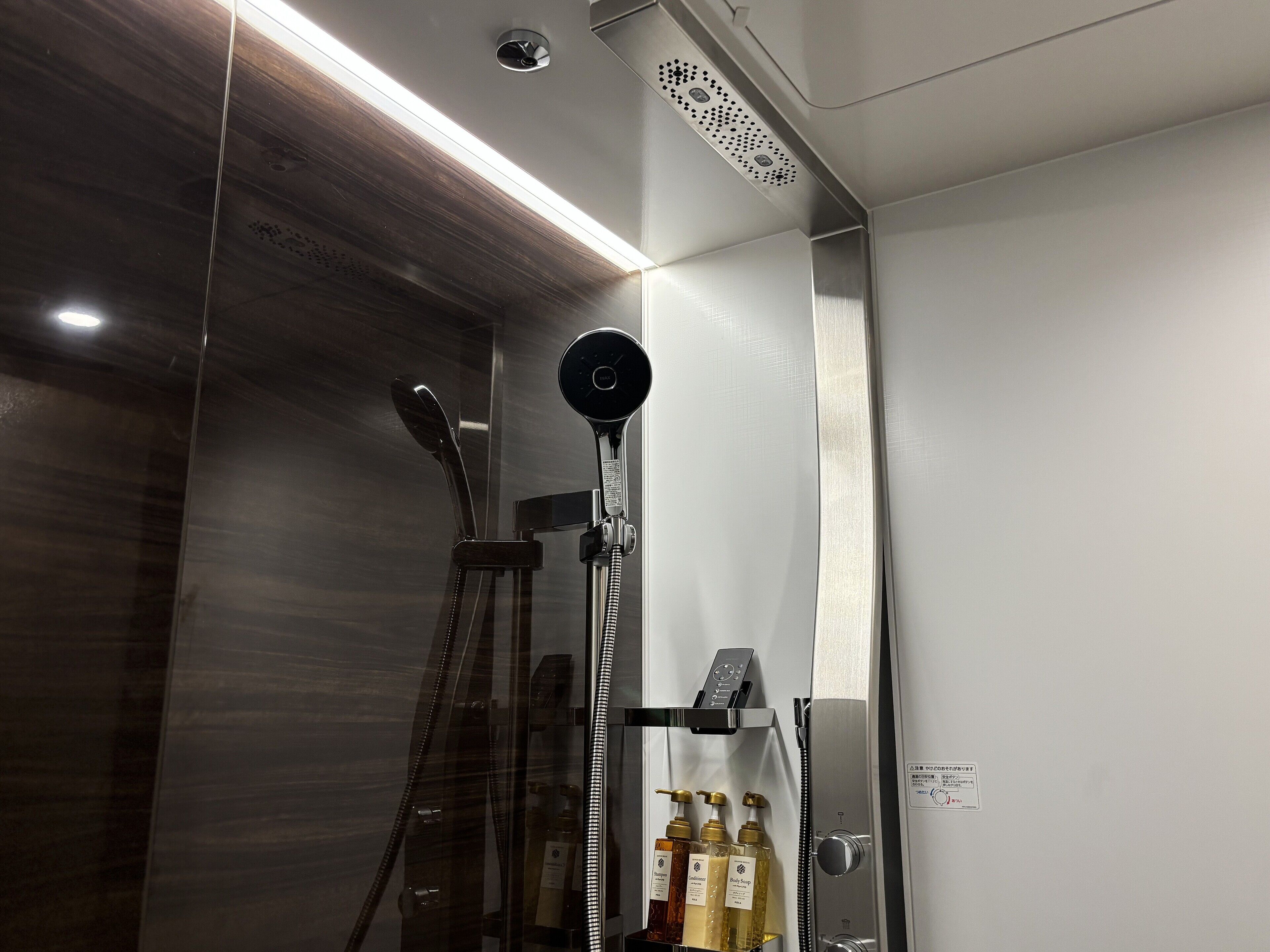 Ein modernes Badezimmer mit einer Glaskabine, einer Handbrause und einem an der Wand montierten Bedienfeld.