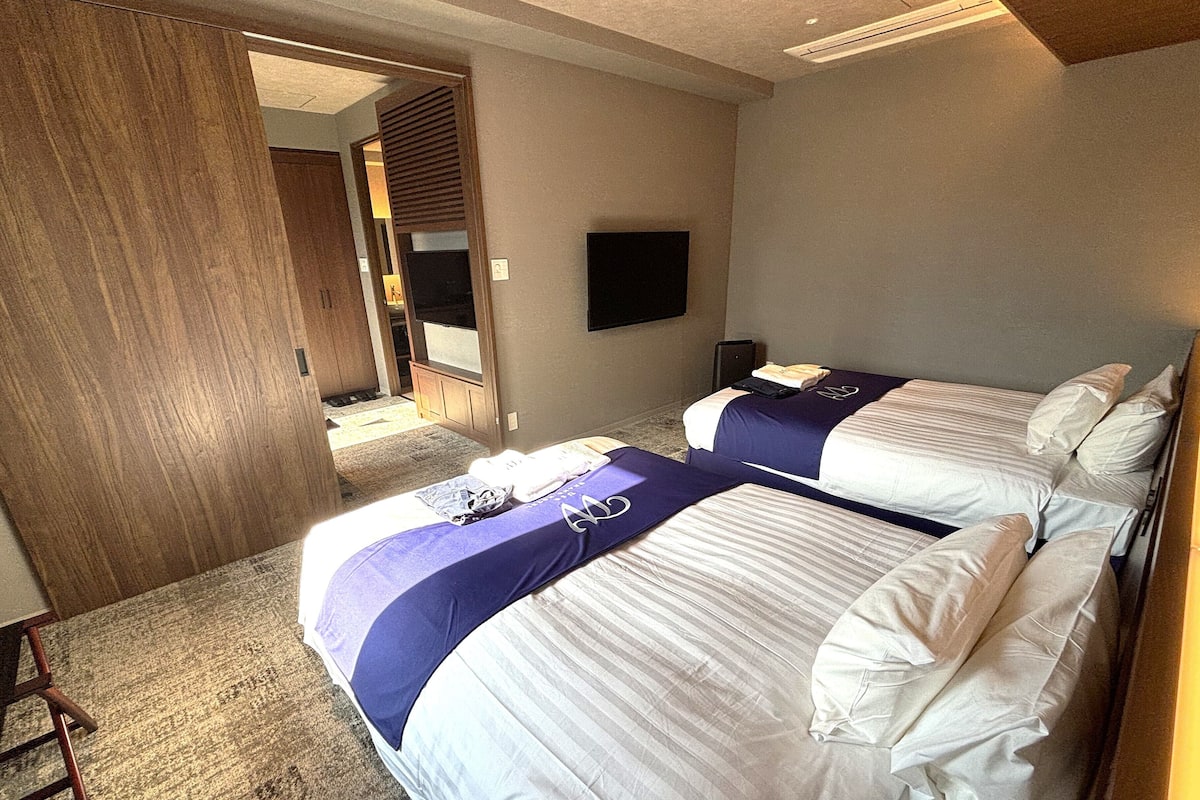 A hotel room with two beds, a TV, and a wooden door.