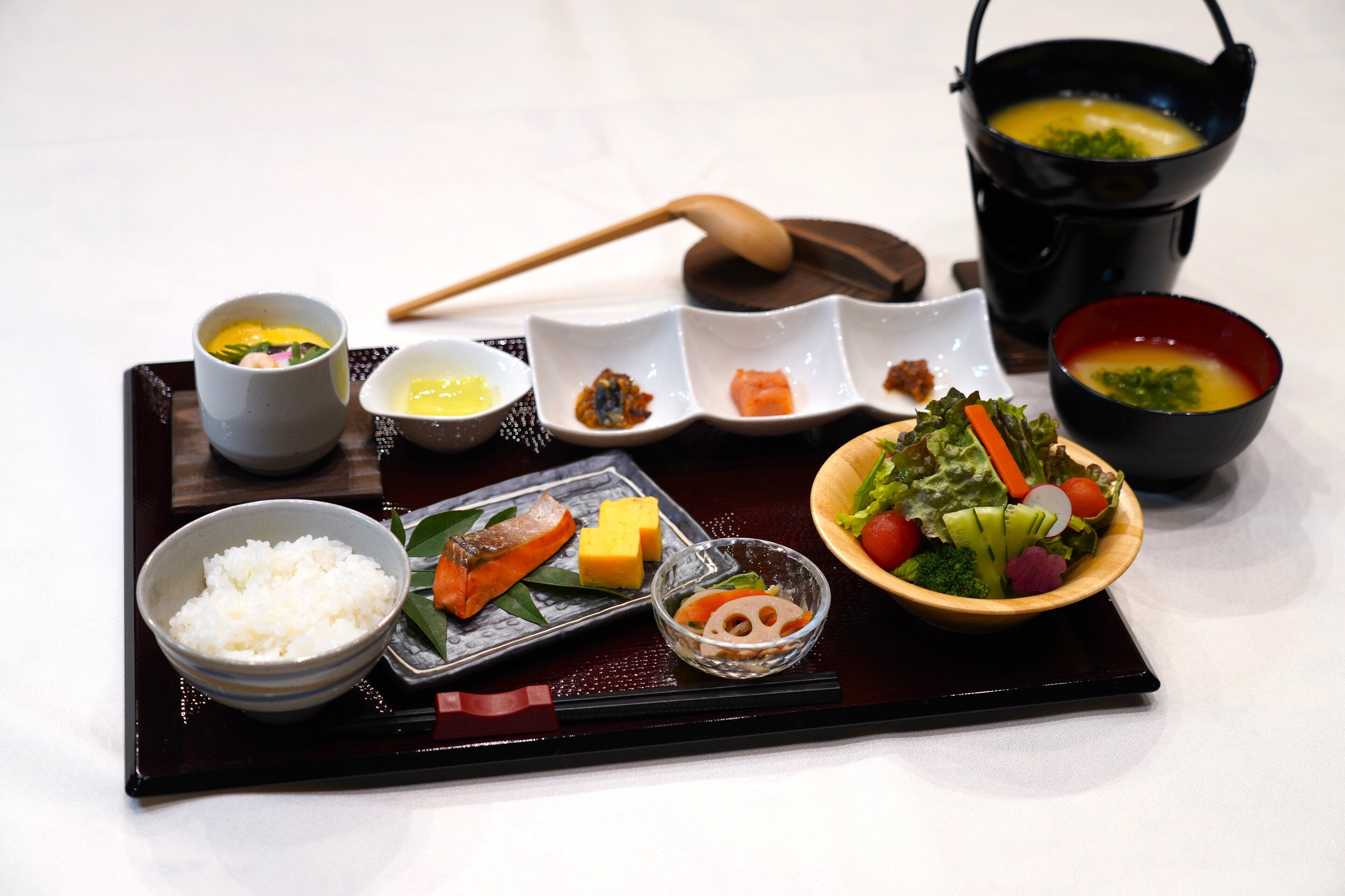 A traditional Japanese meal with rice, fish, vegetables, and soup served on a black tray.