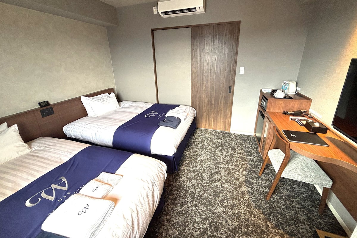 A hotel room with two beds, a desk, a chair, a TV, and a wardrobe.