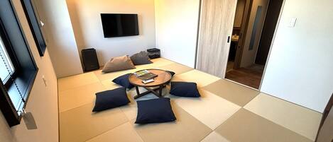 A modern living room with tatami flooring, a round coffee table, and a flat-screen TV mounted on the wall.