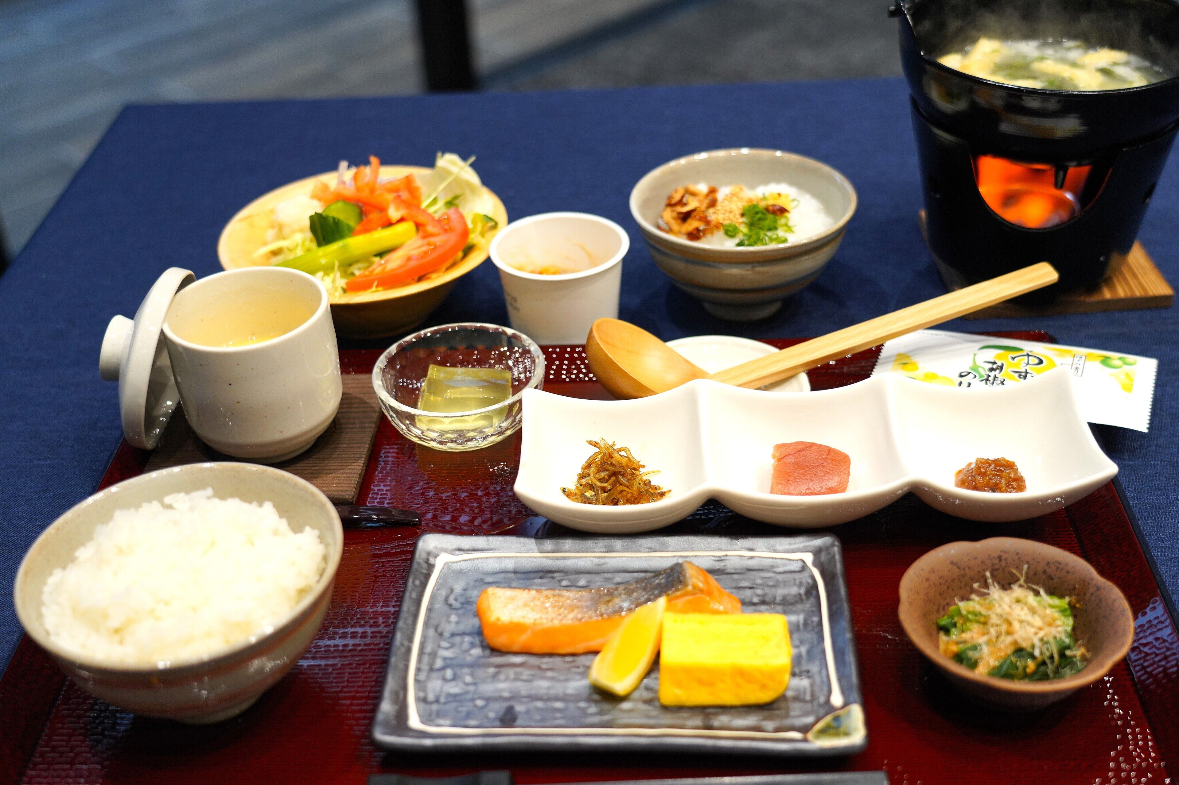 A table with various dishes, including rice, vegetables, and a pot of soup.