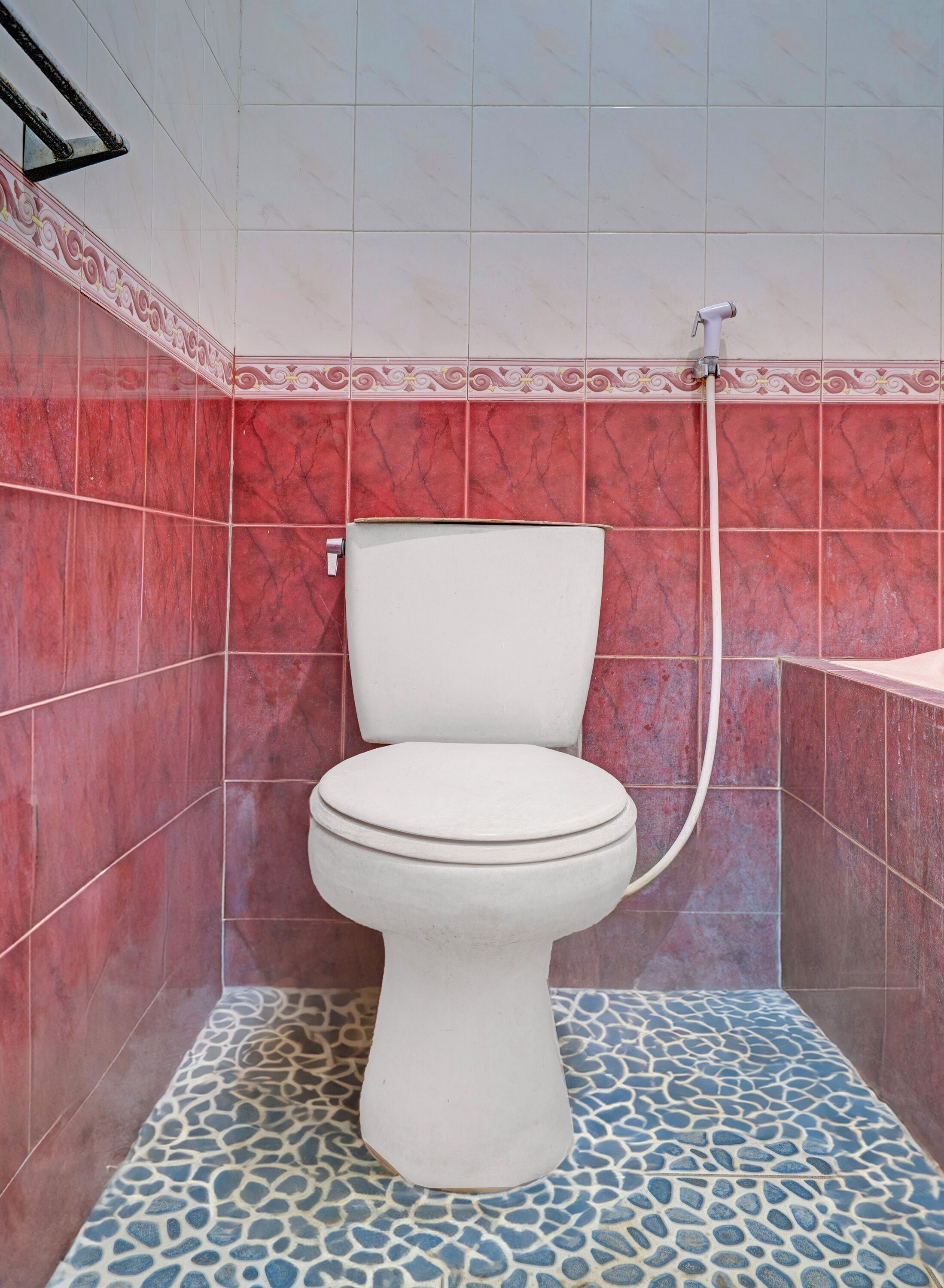 A bathroom with a toilet, red tiled walls, and a patterned floor.