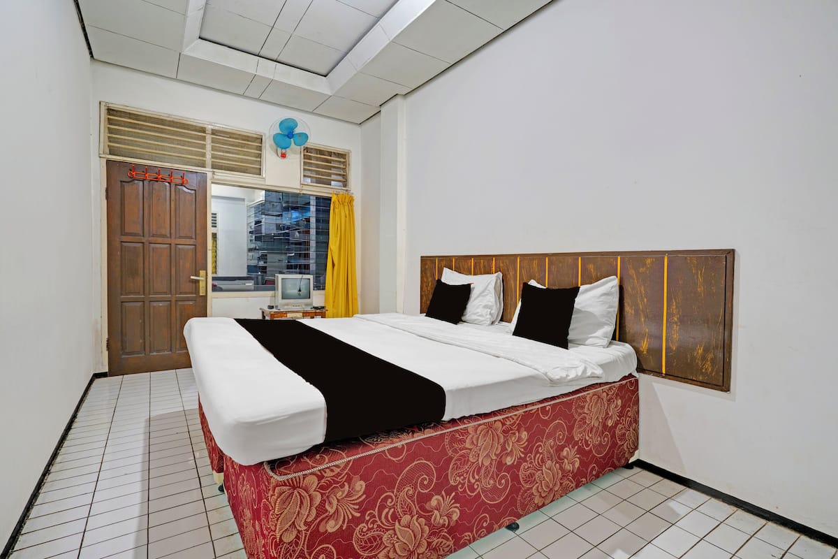A hotel room with a bed, a window with yellow curtains, a wooden door, and a ceiling fan.