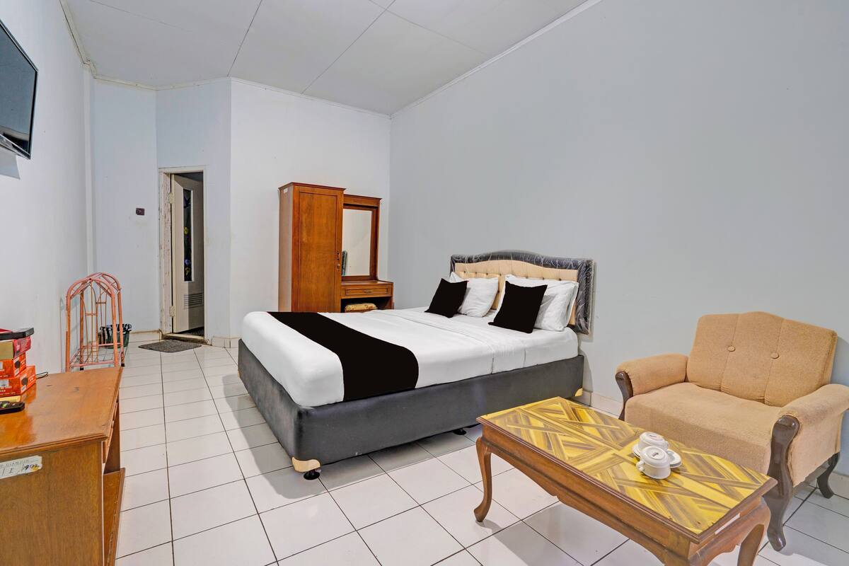 A bedroom with a bed, a wooden dresser, a chair, and a small table.